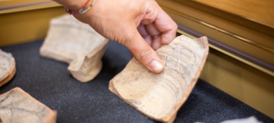 una mano che dispone un pezzo di un'antica ceramica all'interno di espositore da museo